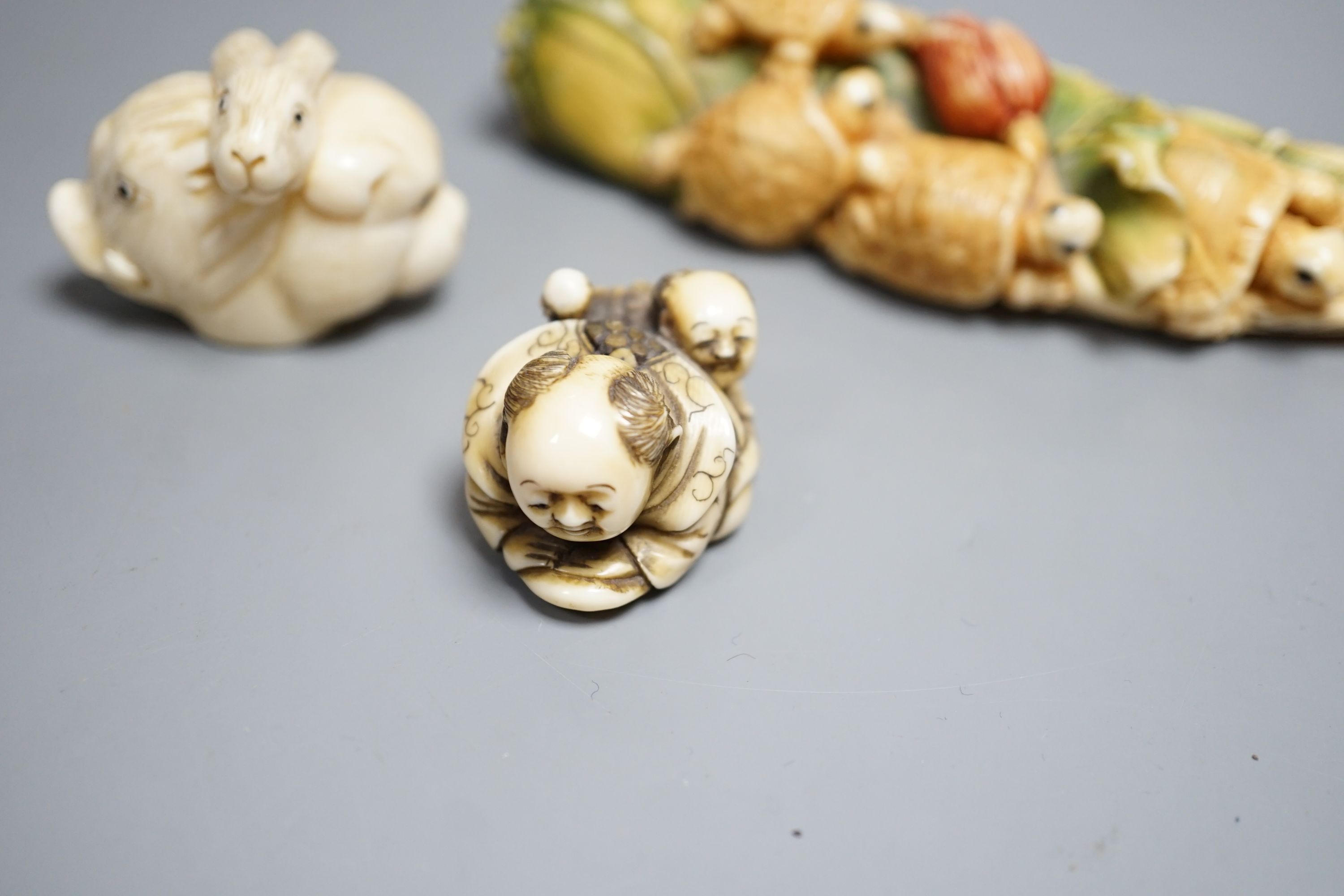 A Japanese ivory Netsuke of two boys holding a noh mask, an ivory Netsuke in the form of three animal heads and a coloured Ivory carving of tortoises on a lotus leaf, all singed (3) largest 12cm